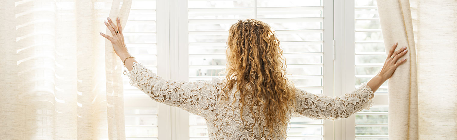 Woman looking out big bright window with blinds